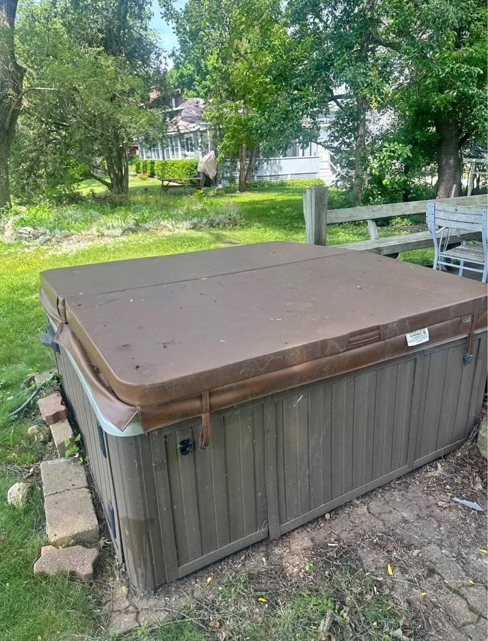 Before: an old brown hot tub with a weathered cover on a paver patio beside a deck
